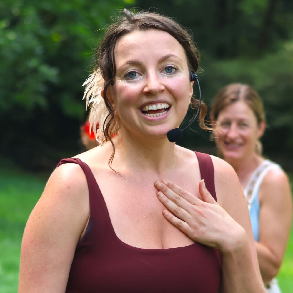 Amy Dickens smiling and speaking into a headset microphone while outdoors at a park event